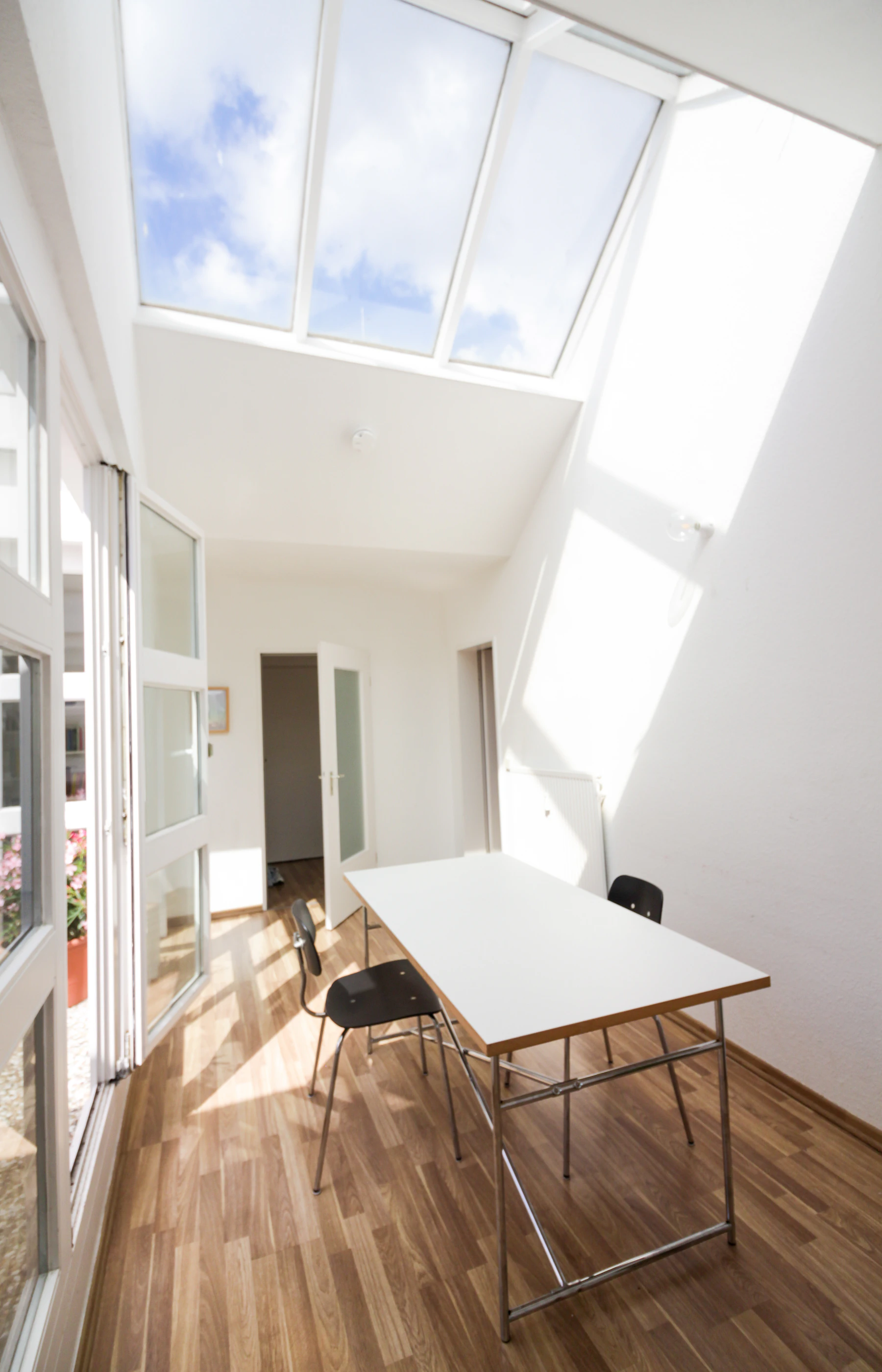 Une verrière éclaire les murs clairs et le parquet d’une salle à manger