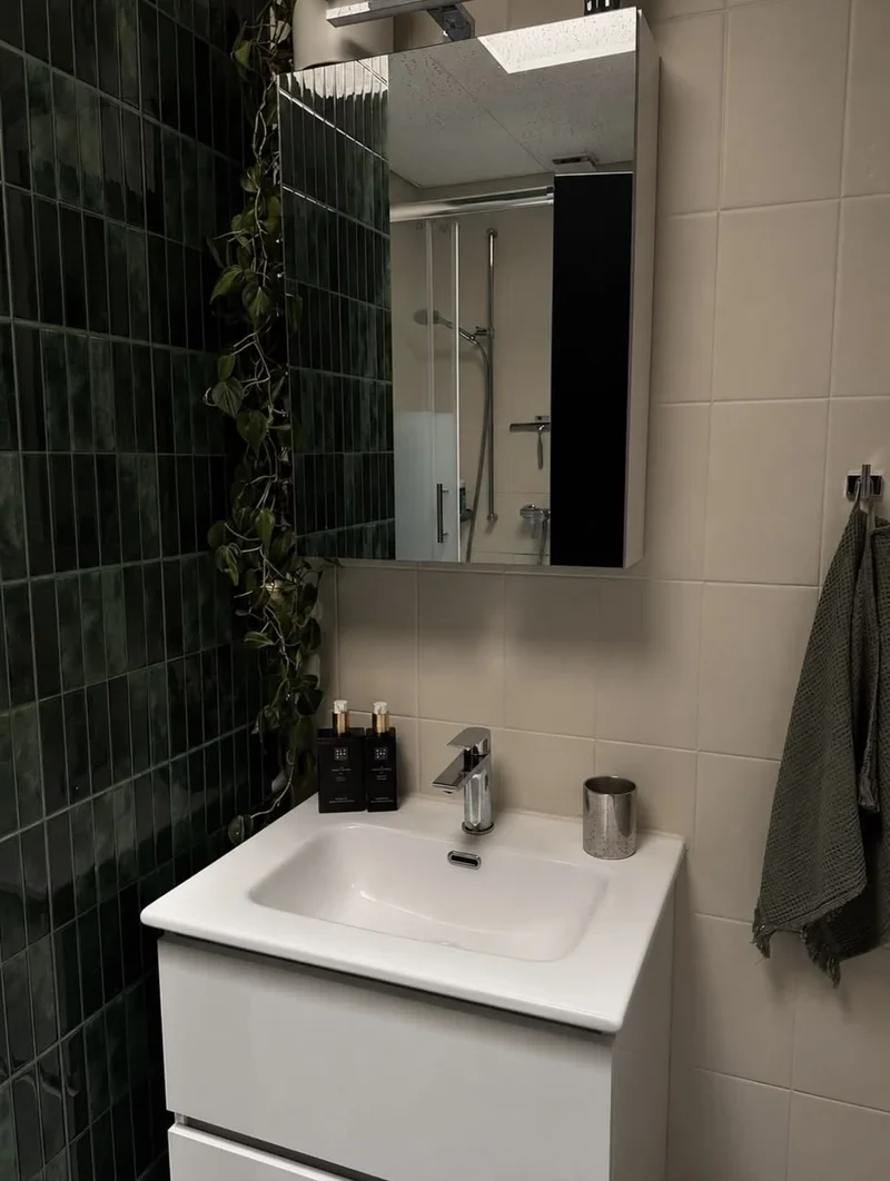 Vasque blanche et miroir à côté d’un mur vert foncé dans une salle de bains